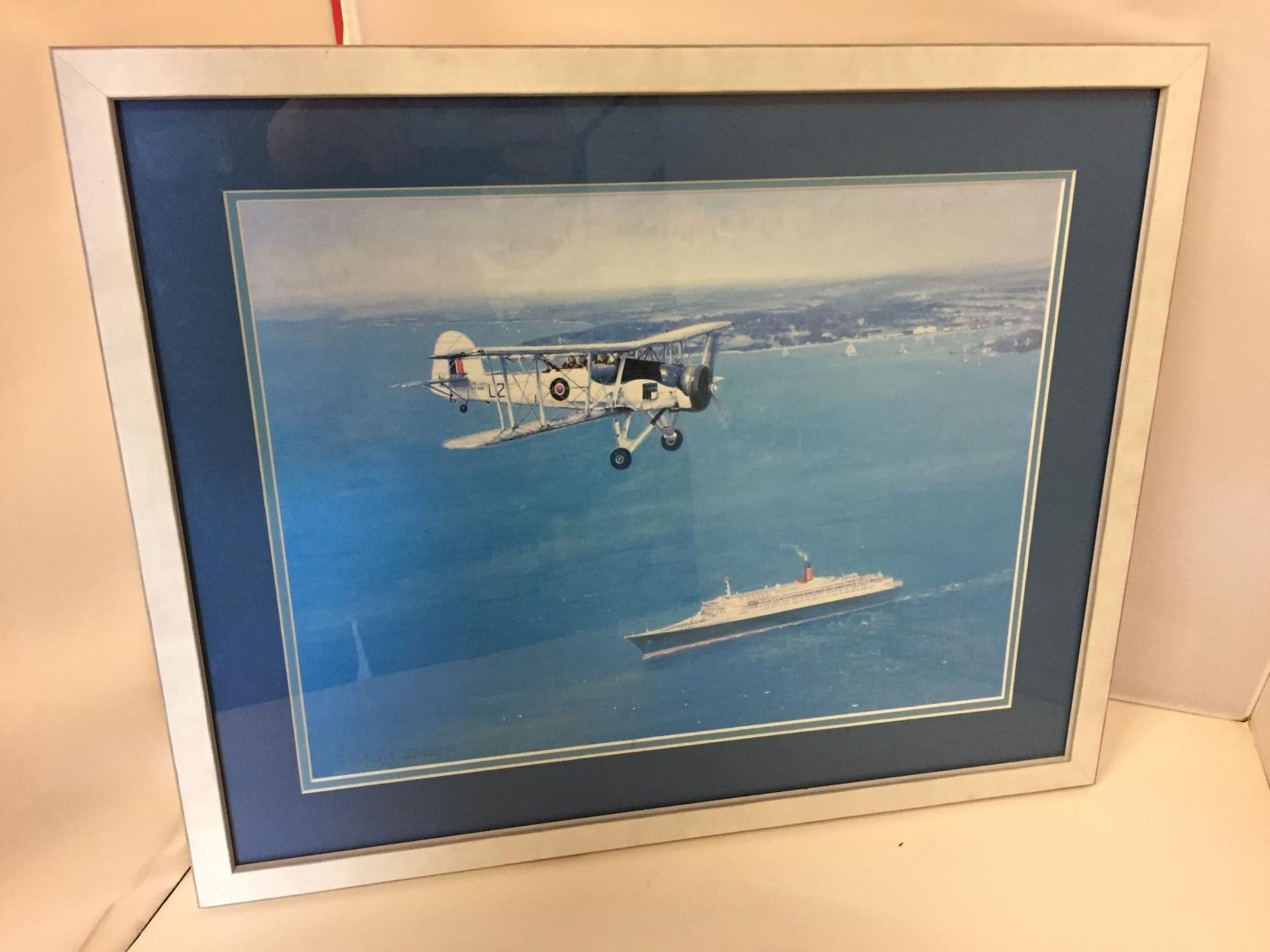 A FRAMED COLOURED PICTURE OF A SWORDFISH PLANE FLYING OVER A CRUISE SHIP 30CM X 40CM