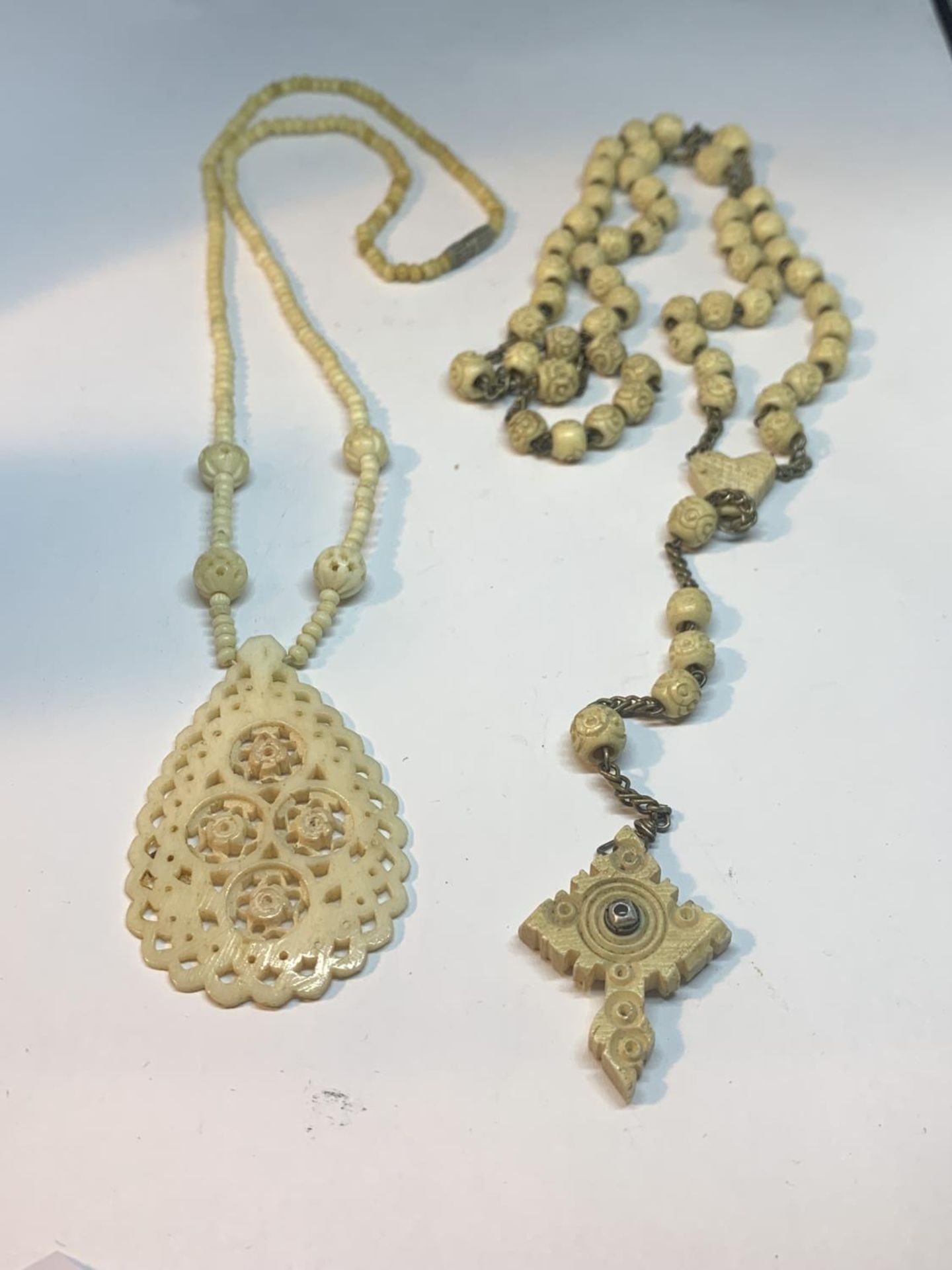 TWO CARVED BONE NECKLACES ONE WITH LARGE FOB AND ONE WITH A CROSS DESIGN