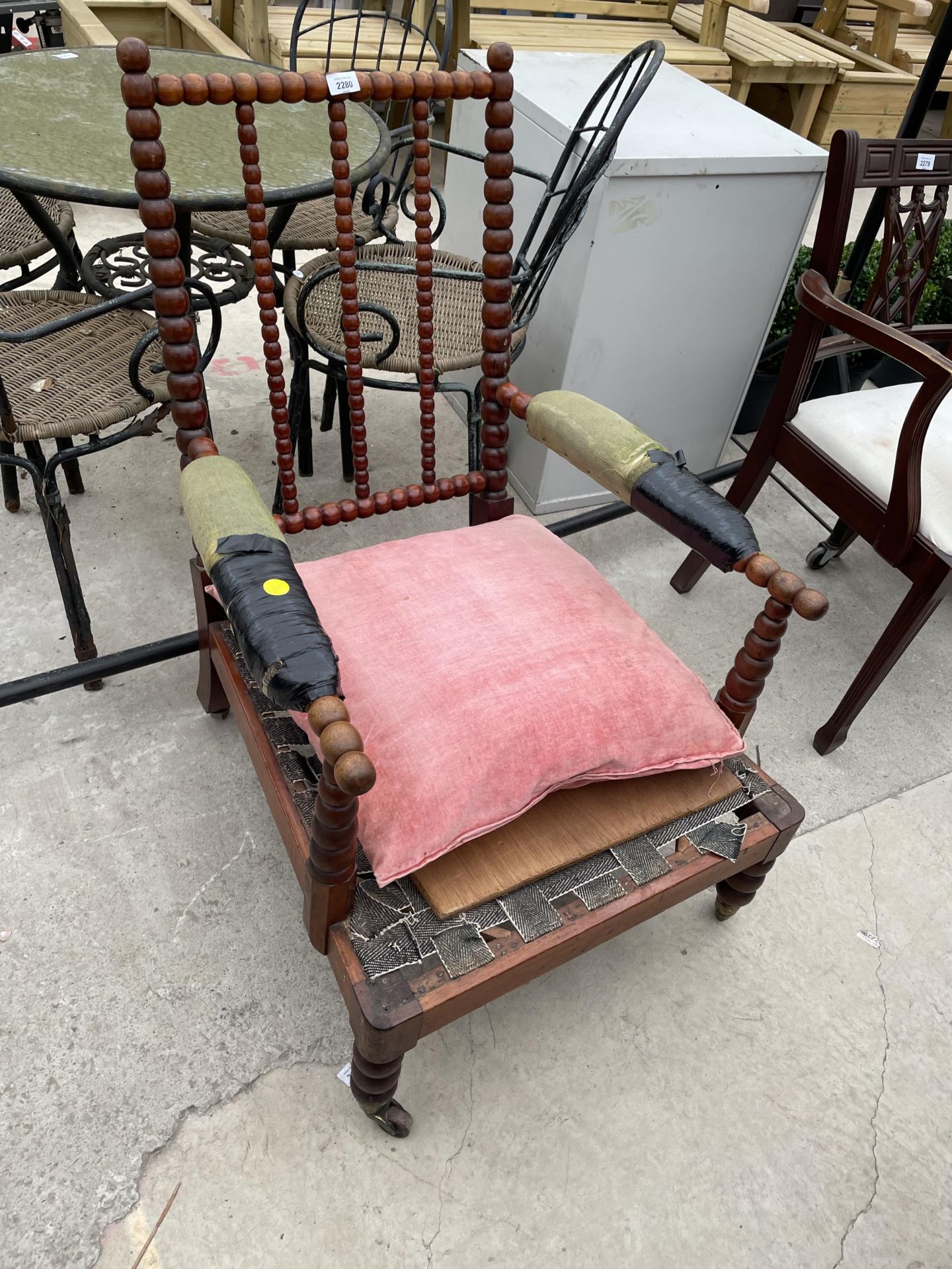 A 19TH CENTURY BOBBIN TURNED FIRESIDE CHAIR WITH SLOPING BACK, ON PORCELAIN/BRASS CASTERS