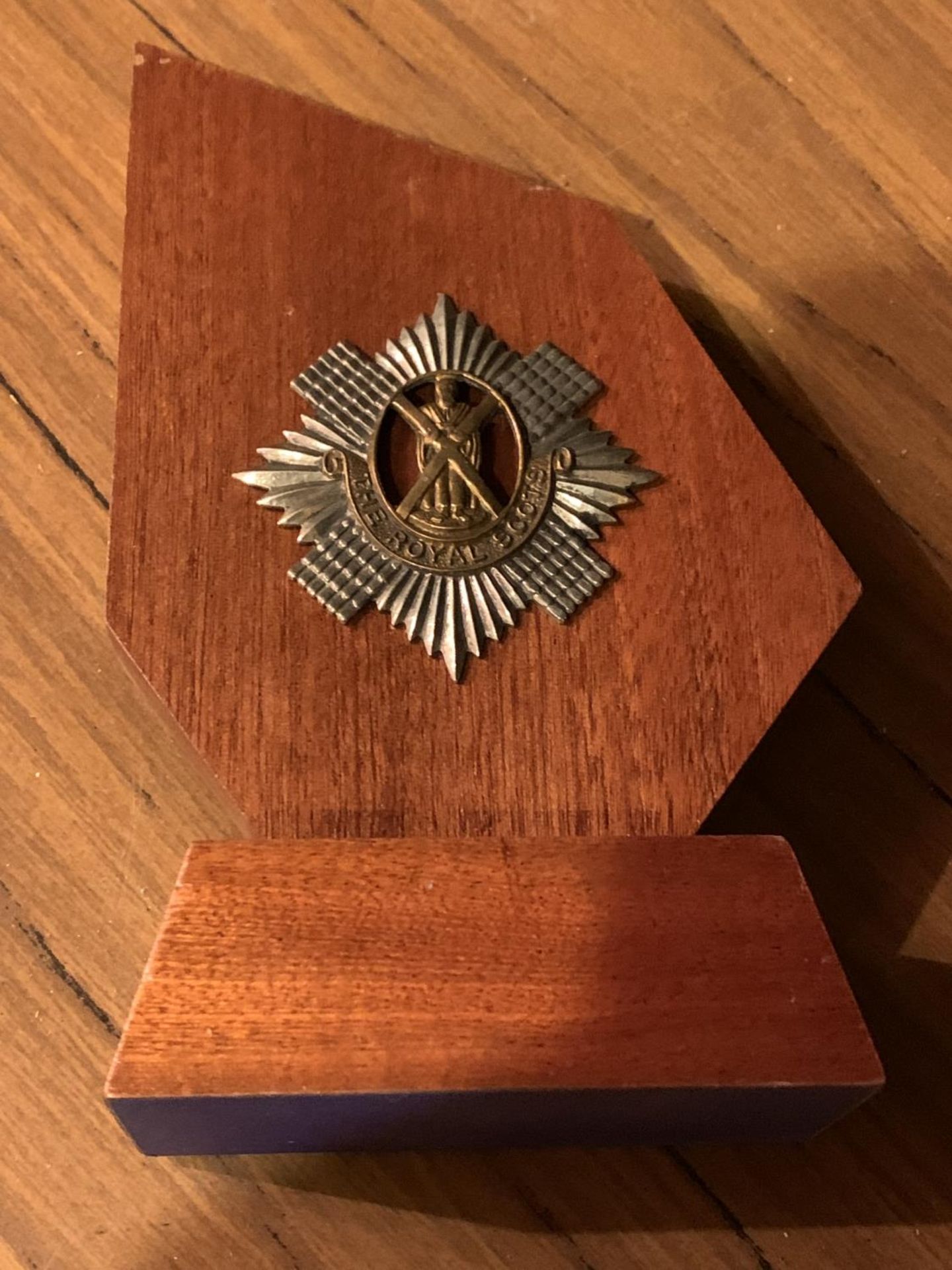 A ROYAL SCOTS BADGE ON A WOODEN MOUNT
