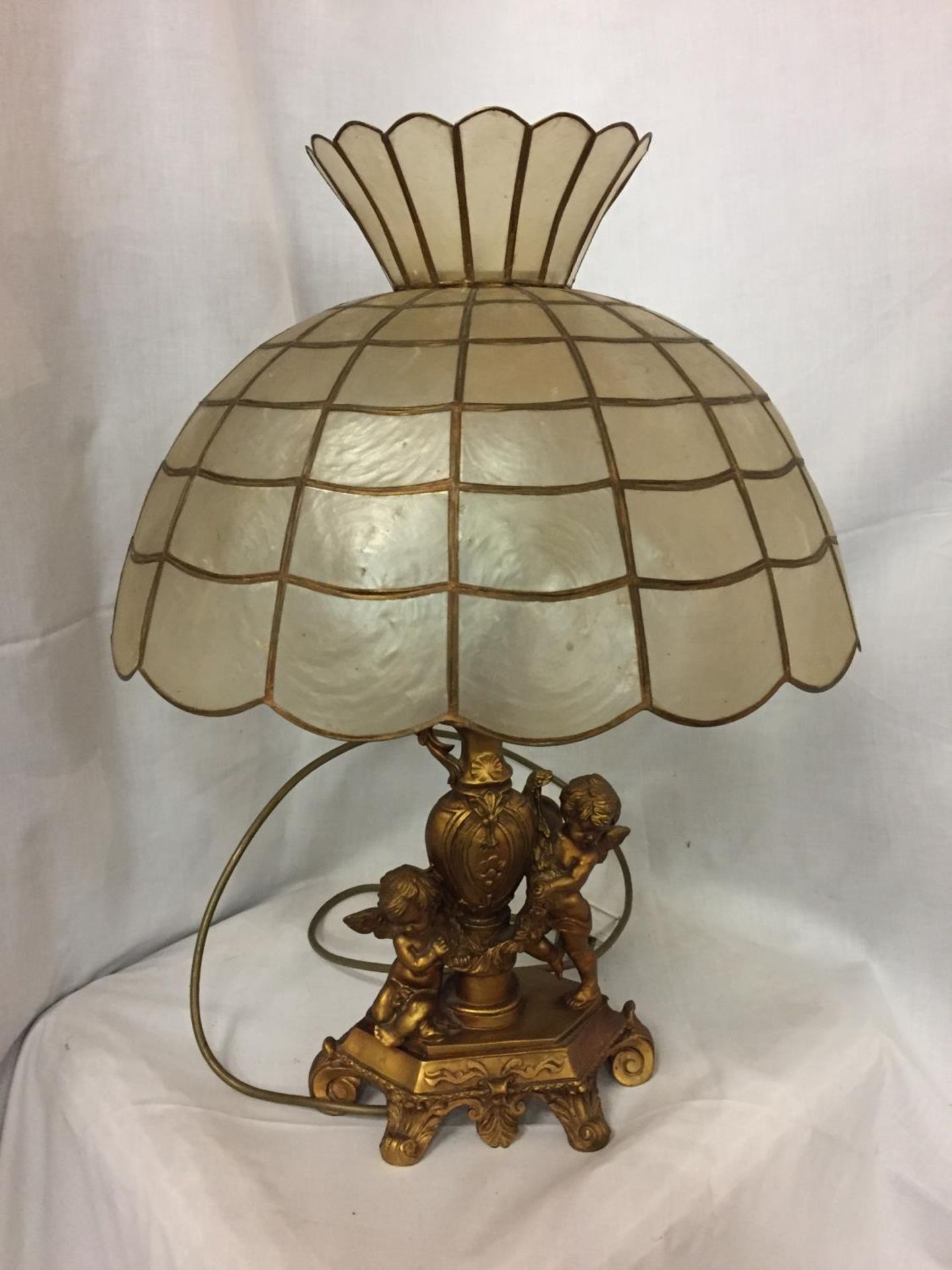AN ORNATE GILDED LAMP BASE DEPICTING CHERUBS WITH A CAPIZ SHELL SHADE