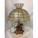 AN ORNATE GILDED LAMP BASE DEPICTING CHERUBS WITH A CAPIZ SHELL SHADE