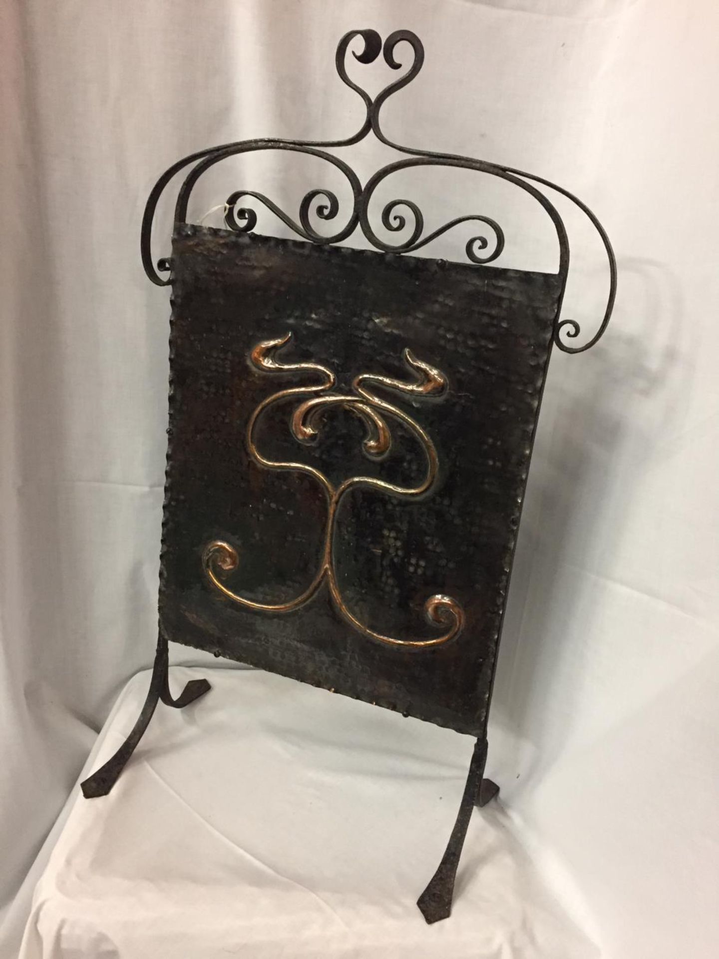AN ARTS AND CRAFTS FIRE SCREEN WITH A DECORATIVE COPPER PANEL ON A WROUGHT IRON FRAME