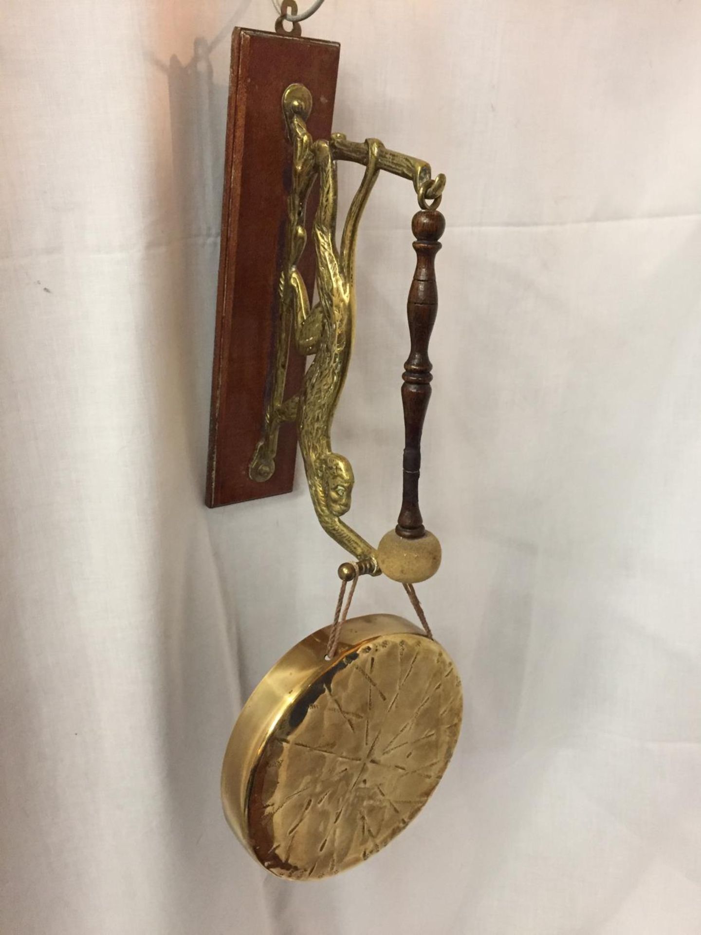 A BRASS MONKEY WALL MOUNTED DINNER GONG ON WOODEN PLINTH