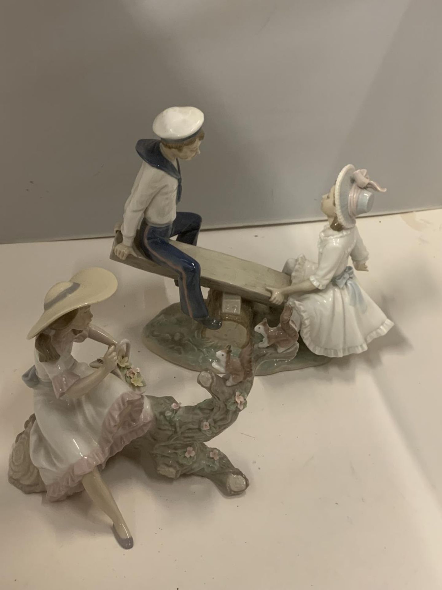 TWO LLADRO FIGURINES, ONE OF A BOY AND GIRL ON A SEE-SAW, THE OTHER OF A GIRL WITH A BASKET OF