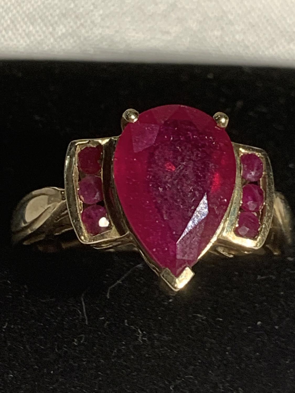 A 9 CARAT GOLD RING WITH A LARGE RED STONE AND THREE SMALL STONES EACH SIDE SIZE R GROSS WEIGHT 4.