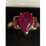 A 9 CARAT GOLD RING WITH A LARGE RED STONE AND THREE SMALL STONES EACH SIDE SIZE R GROSS WEIGHT 4.