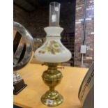 A BRASS BASED OIL LAMP WITH A CLEAR GLASS CHIMNEY AND A FLORAL GLASS SHADE