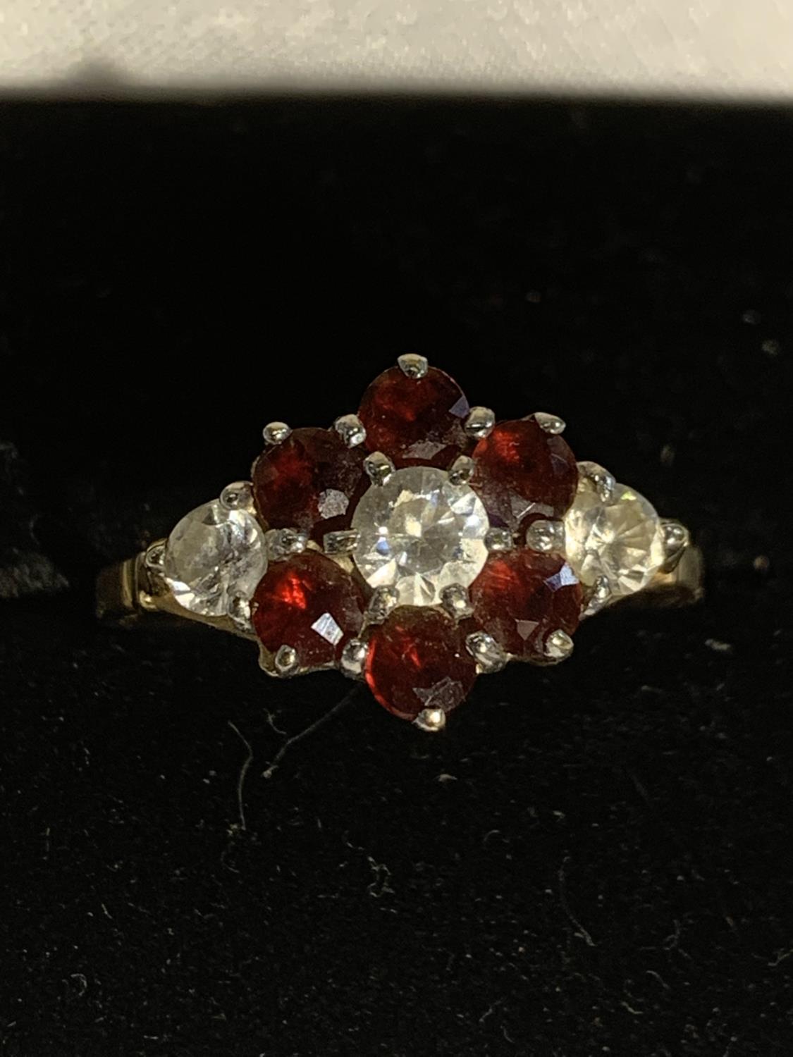 A 9 CARAT GOLD RING WITH THREE CLEAR STONES AND SIX RED STONES IN A FLOWER DESIGN SIZE Q GROSS