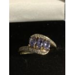 A 9 CARAT GOLD RING WITH THREE IN LINE PURPLE STONES AND POSSIBLY DIAMOND CHIPS TO THE SHOULDER SIZE