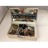 A CREAM COLOURED MIRRORED JEWELLERY BOX CONTAINING COSTUME JEWELLERY TO INCLUDE WATCHES, RINGS,
