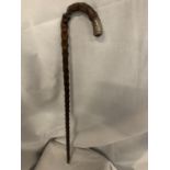 A TEXTURED WOODEN CANE WITH METAL DEISGN TO THE END OF THE HANDLE. SMALL AMOUNT OF DAMAGE TO THE