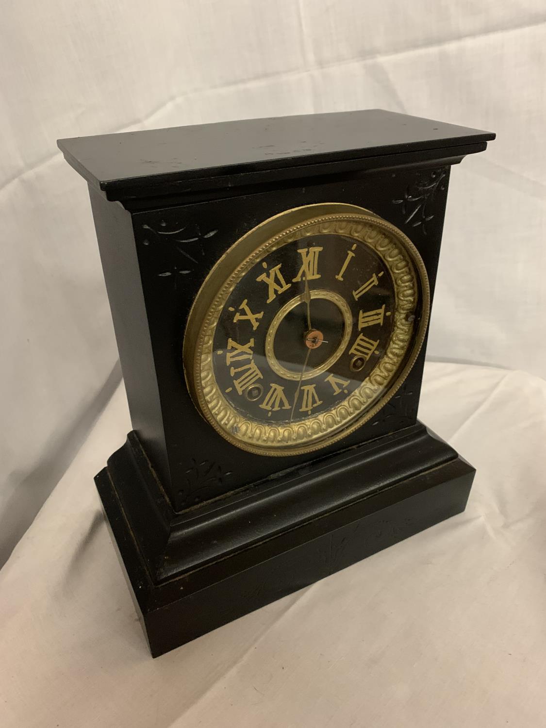 A HEAVY BLACK METAL MANTLE CLOCK WITH GILT ROMAN NUMERALS AND FACE SURROUND