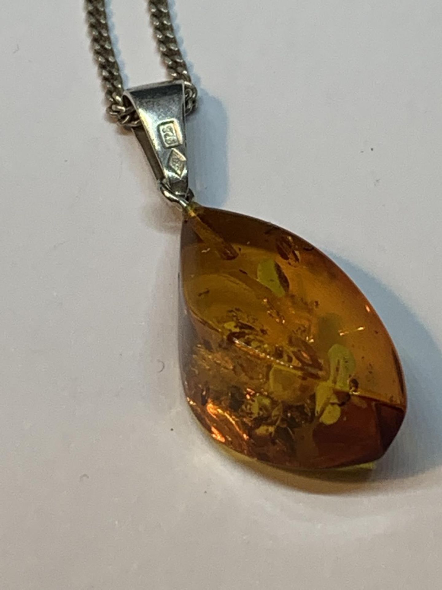 A DECORATIVE SILVER BANGLE WITH A LARGE CENTRAL AMBER STONE AND AN AMBER DROP ON A SILVER CHAIN IN A - Image 4 of 4