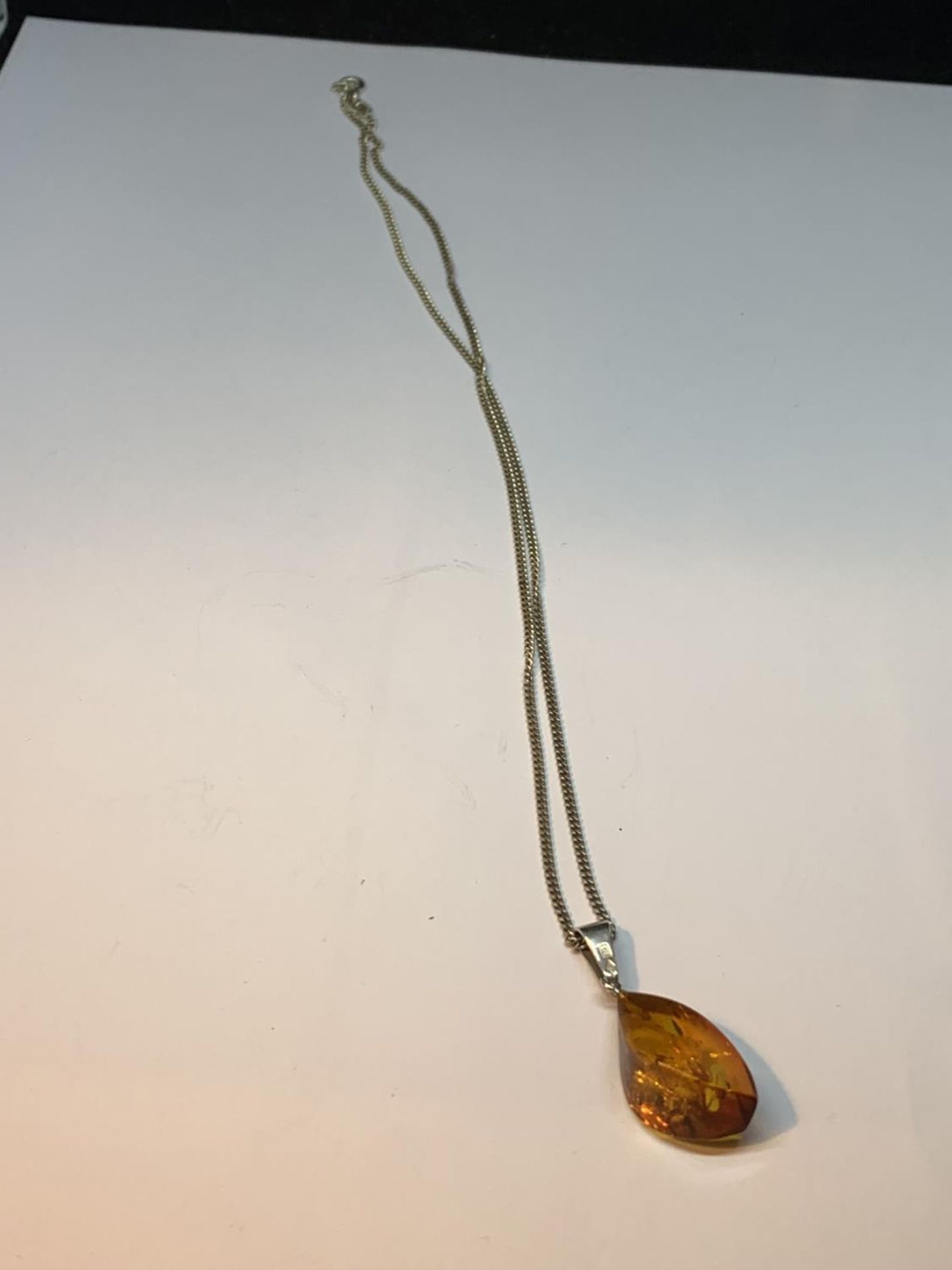 A DECORATIVE SILVER BANGLE WITH A LARGE CENTRAL AMBER STONE AND AN AMBER DROP ON A SILVER CHAIN IN A - Image 3 of 4
