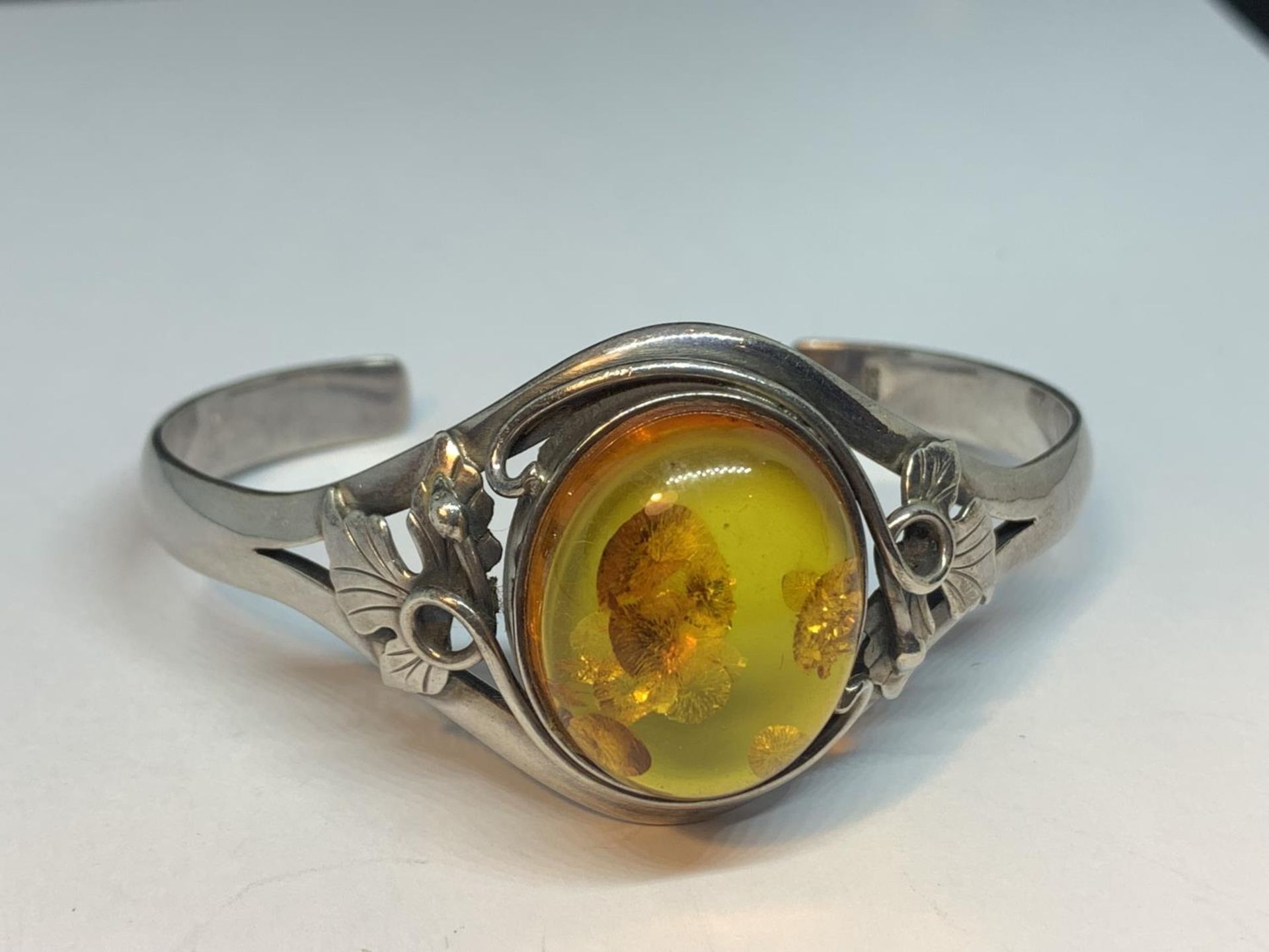 A DECORATIVE SILVER BANGLE WITH A LARGE CENTRAL AMBER STONE AND AN AMBER DROP ON A SILVER CHAIN IN A - Image 2 of 4