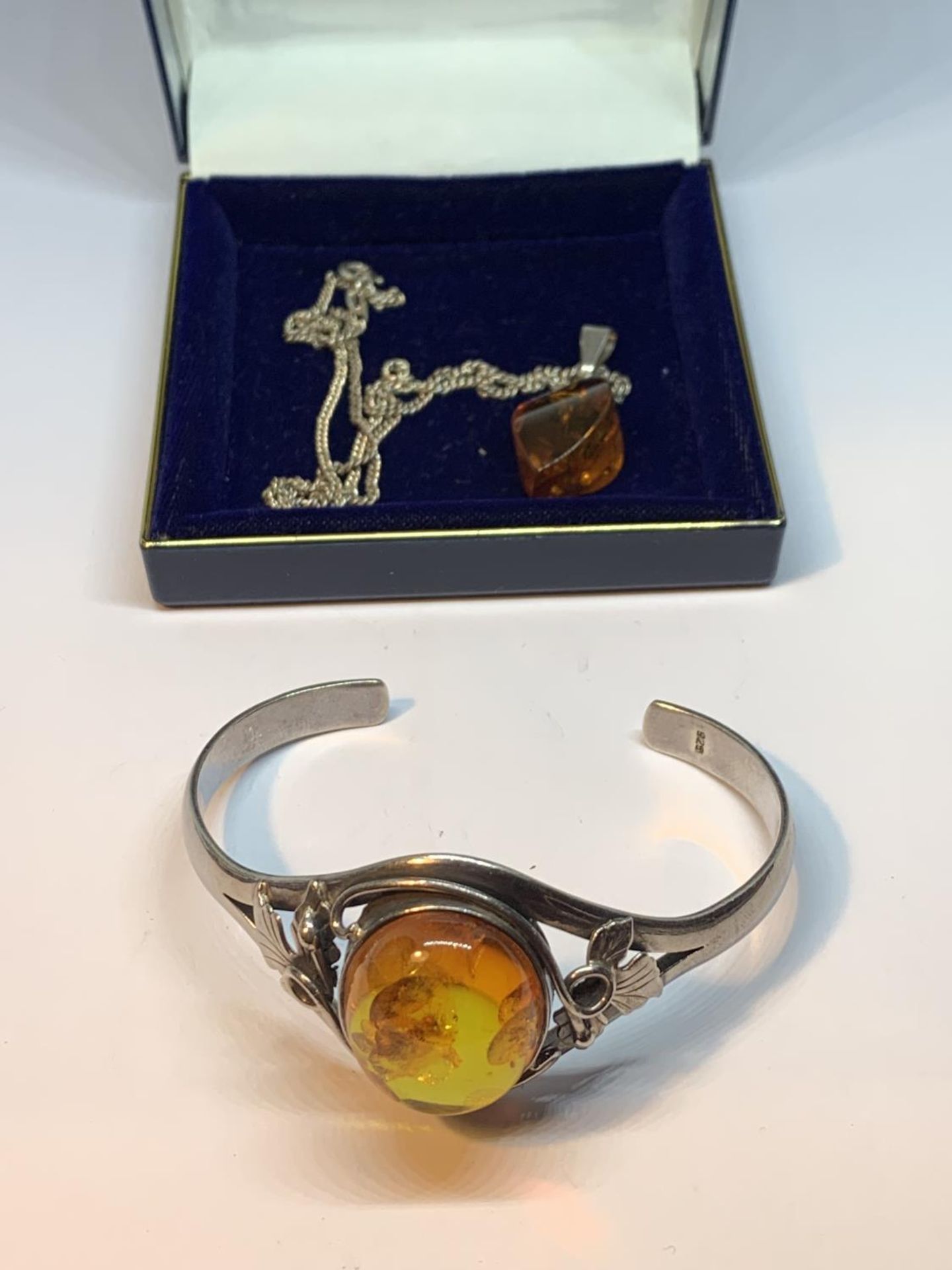 A DECORATIVE SILVER BANGLE WITH A LARGE CENTRAL AMBER STONE AND AN AMBER DROP ON A SILVER CHAIN IN A