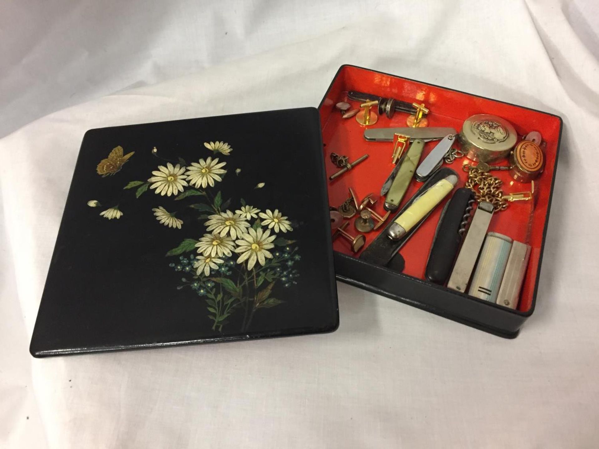 AN ORIENTAL SYLE LACQUERED BOX CONTAINING COLLECTABLES TO INCLUDE PEN KNIVES, CUFFLINKS AND PILL