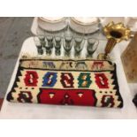 A RED PATTERNED RUG, SMOKY GLASSES AND A BRASS VASE