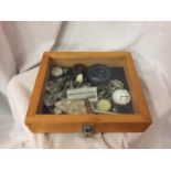 A GLASS LIDDED DISPLAY CABINET CONTAINING COLLECTIBLES TO INCLUDE WATCHES, POKER DICE, DECANTER