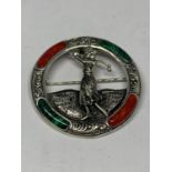 A MARKED SILVER CIRCULAR BROOCH WITH GREEN AND RED STONES DEPICTING A LADY GOLFER