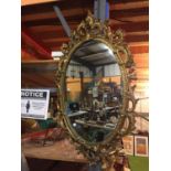 AN ORNATE GILDED OVAL MIRROR