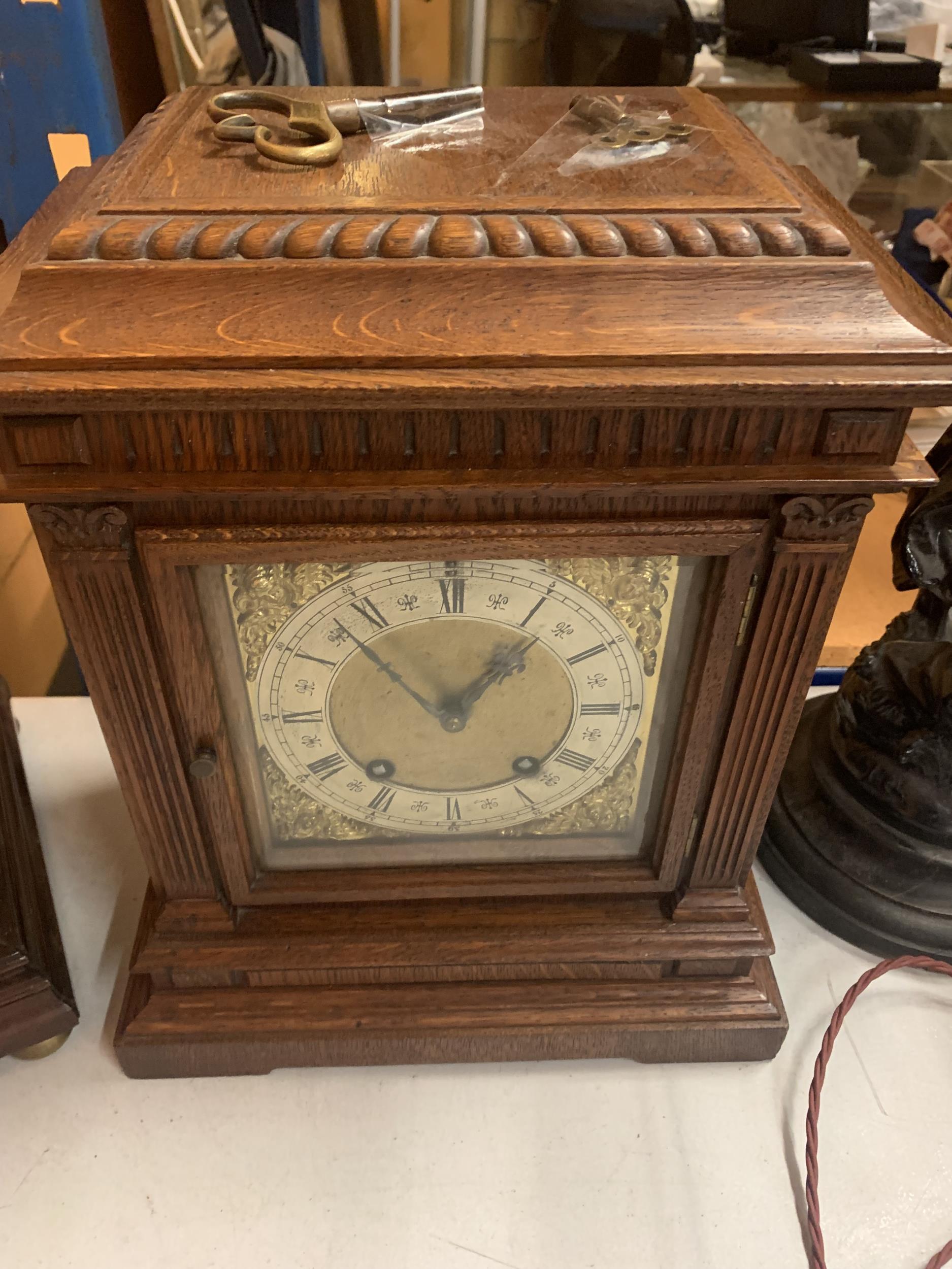 AN OAK CASED CHIMING MANTLE CLOCK WITH DECORATIVE GILT FACE WITH ROMAN NUMERALS COMPLETE WITH BOTH