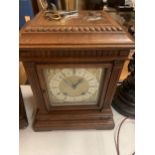 AN OAK CASED CHIMING MANTLE CLOCK WITH DECORATIVE GILT FACE WITH ROMAN NUMERALS COMPLETE WITH BOTH