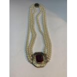 A PEARL AND SILVER GILT THREE STRAND NECKLACE WITH A LARGE RED CENTRE STONE