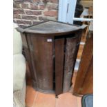 A GEORGIAN OAK BOW FRONTED CORNER CUPBOARD WITH BRASS H-HINGES (REQUIRES REPAIR TO DOOR)