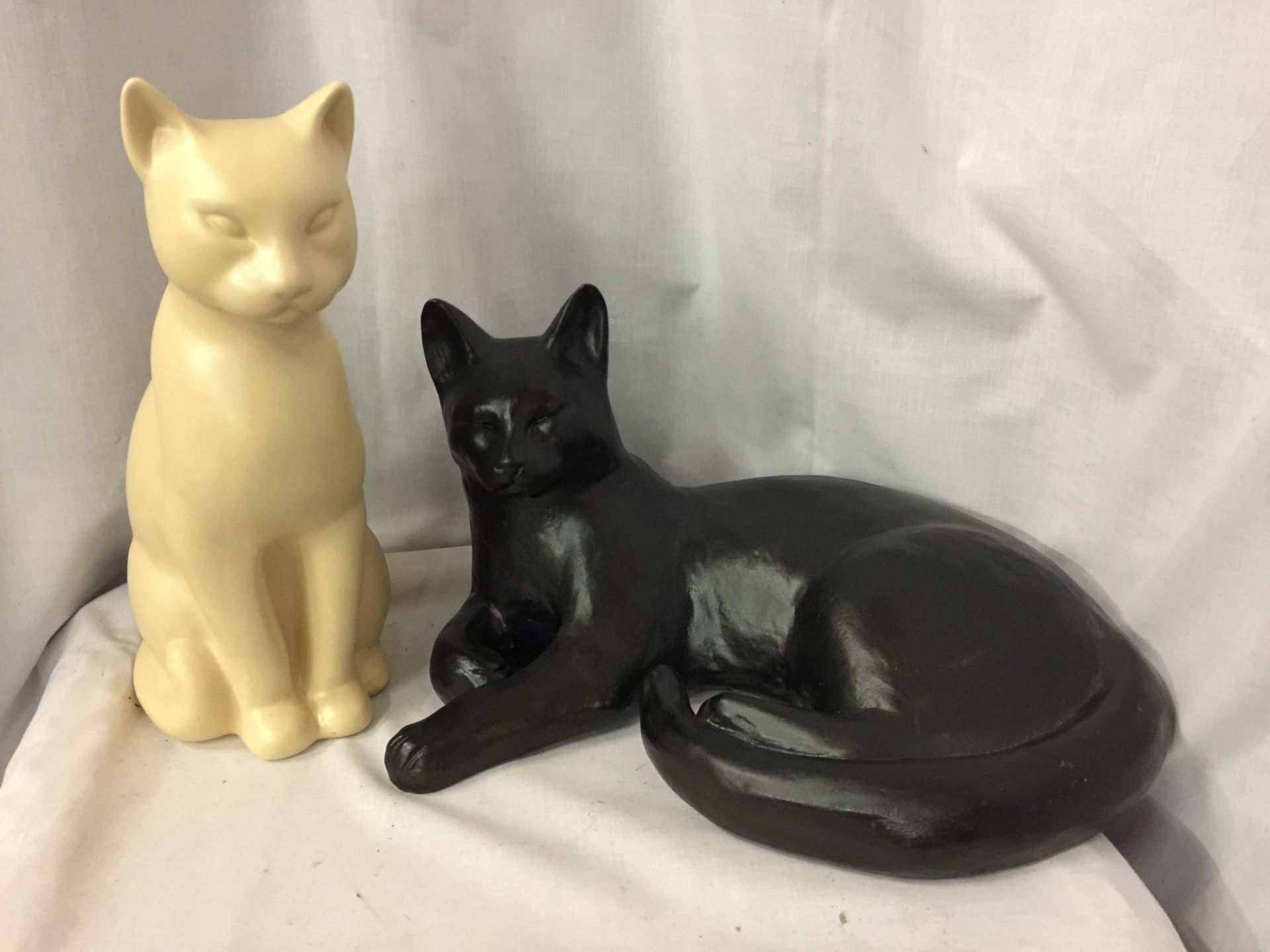 TWO LARGE CAT FIGURES, ONE BLACK, LYING DOWN, LENGTH 36CM, AND A CREAM ONE, HEIGHT 30CM