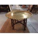 A LARGE DECORATIVE BRASS CHARGER WITH PIE CRUST EDGING ON WOODEN STAND, DIAMETER 67CM, HEIGHT 42CM