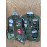 A PAIR OF BARBOUR ZIP UP BODY WARMERS DECORATED WITH VARIOUS FISHING BADGES AND TO ALSO INCLUDE