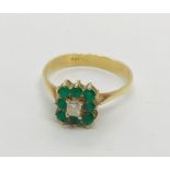 An 18ct gold ring set with a cluster of emeralds around a radiant cut diamond