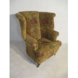 A modern upholstered winged back arm chair on turned legs