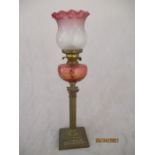 A Victorian oil lamp with Corinthian column with cranberry coloured well and shade