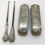 Two silver handled boot pulls along with two silver backed brushes