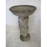 A concrete birdbath with base of semi-nude ladies