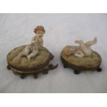 A pair of Edwardian bisque cherubs seated on cushions with ivory feet