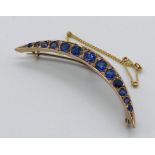 A 9ct gold crescent shaped brooch set with graduated sapphire coloured stones