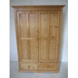 A modern pine double wardrobe with panelled doors and two drawers under