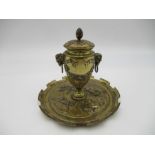 A brass ink well decorated with classical scenes, featuring rams head handles