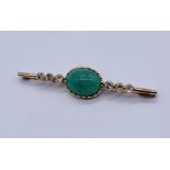 An unmarked gold brooch ( tested 14ct) set with an emerald coloured cabochon flanked by diamonds