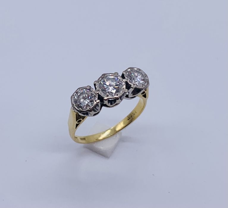 A diamond three stone ring set in 18ct gold, illusion set, the centre diamond appears to measure