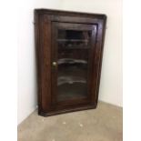 An oak hanging corner cupboard with glazed door and shelves.W:71cm x D:35cm x H:101cm