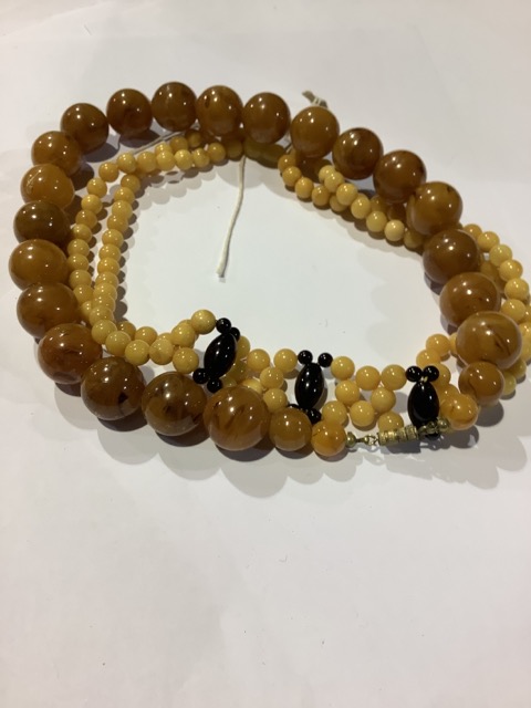 A string of amber beads together with a large strand of faux amber beads.