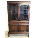 An oak two piece bookcase over cupboard and two drawers with carved cornice on barley twist legs.