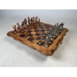 A wooden chess board with four feet plus metal chess pieces. One broken and foot missing from