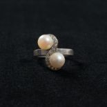 An unmarked platinum and diamond pearl crossover ring. Set with two 7mm cultured pearls with a