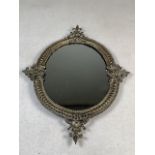 An ornate small brass oval wall mirror with brass back.